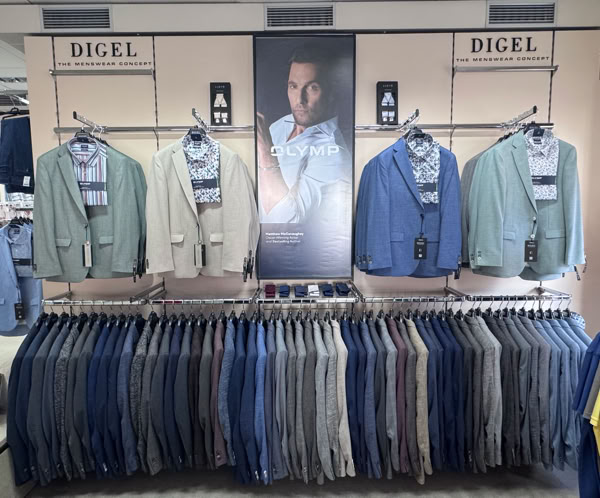 Kleiderständer mit verschiedenen Anzügen und Hosen in Blau- und Beigetönen, darüber ein großes Foto eines Mannes in einem Anzug.